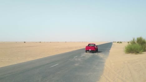 Red-truck-driving-down-empty-desert-road,-tracking-from-behind