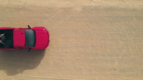 Red-truck-driving-on-a-sandy-desert-track,-enters-the-frame-to-down-view