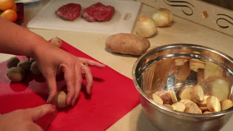 Woman-slicing-baby-potatoes-with-chef-knife-and-red-cutting-board