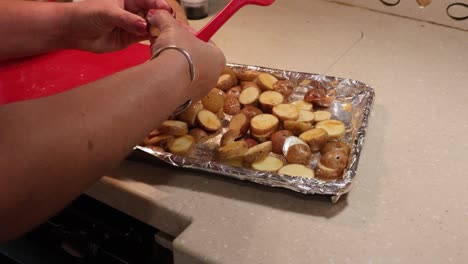 Close-up-of-woman-breaking-up-and-laying-flat-sliced-baby-potatoes-on-a-pan-ready-for-roasting-in-an-RV-kitchen