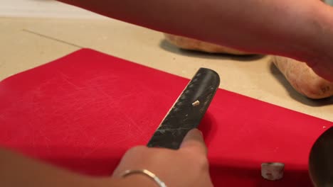 Close-up-of-the-hands-of-a-woman-slicing-button-mushrooms-using-a-Japanese-chef-knife-and-a-red-cutting-board