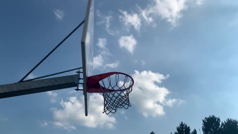 Basketball-ball-entering-the-rim-and-falling-through-the-net,-against-the-blue-sky