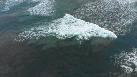 Eine-Luftaufnahme-Aus-Der-Luftbahn-Aus-Der-Vogelperspektive-Einer-Weißen-Wellenwäsche,-Die-über-Ein-Riff-Im-Blauen-Wasser-Vor-Der-Küste-Australiens-Wäscht
