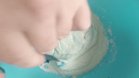 Mixing-blue-food-colouring-to-sponge-cake-batter-mixture-top-down-view
