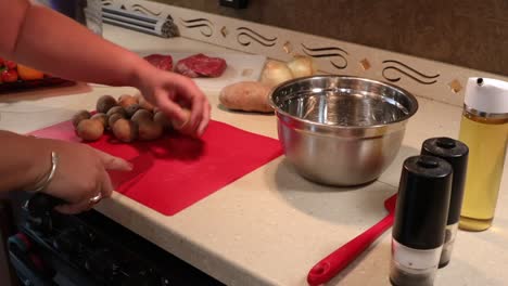 Woman-picking-up-chef-knife-to-slice-baby-potatoes-and-put-the-pieces-into-stainless-steel-bowl