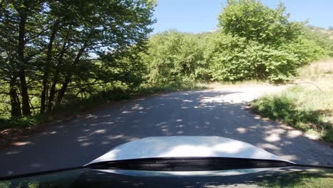 Fahrer-Pov-Von-Einem-Weißen-Auto,-Das-Auf-Der-Bergstraße-Rechts-Abbiegt,-Mit-Reflektierender-Windschutzscheibe-Und-Hellem-Sonnenlicht,-Das-Durch-Grüne-Bäume-In-Der-Landschaft-Südeuropas-Scheint