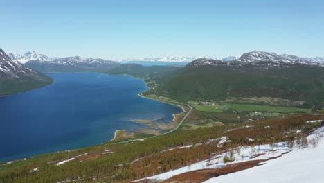 Luftaufnahme-Mit-Blick-Auf-Ein-Dorf-Und-Eine-Straße-An-Der-Küste-Der-Barentssee,-Die-Einen-Riesigen-Felsen-Zeigt,-Sonniger-Sommertag,-In-Rotsund,-Troms,-Nordland,-Norwegen---Rückseite,-Drohnenaufnahme