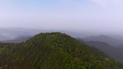 Lush-Green-Mountain-Peak-With-Hazy-Background---orbiting-drone-shot