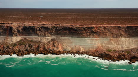 Aerial-dolly-right-shot-of-gigantic-cliff-wall-and-ocean-shore-below-in-summer