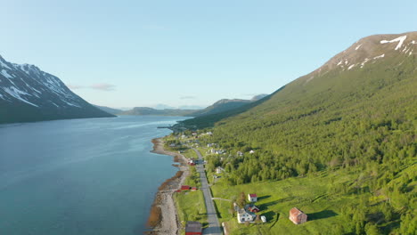 Aerial-view-of-houses,-a-road-and-a-village,-on-the-coast-of-the-Arctic-ocean,-in-middle-of-fjords-and-mountains,-sunny,-summer-day,-in-Rotsund,-Troms,-Nordland,-Norway---descending,-drone-shot