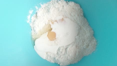Top-view-white-milk-pouring-over-flour-and-eggs-sponge-cake-mixture-in-blue-bowl