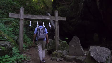 Male-Hiker-Walking-Through-Small-Japanese-Torii-Gate-In-The-Forest---Medium-Shot