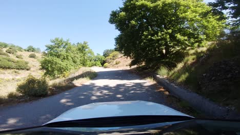 Driver-POV-from-a-white-car-turning-right-on-mountain-road-with-reflective-windshield-and-bright-sunlight-shining-through-green-trees-in-countryside-of-southern-Europe