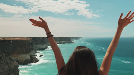 Pretty-woman-rising-hands-up-with-epic-australian-ocean-view-in-background,rear-shot