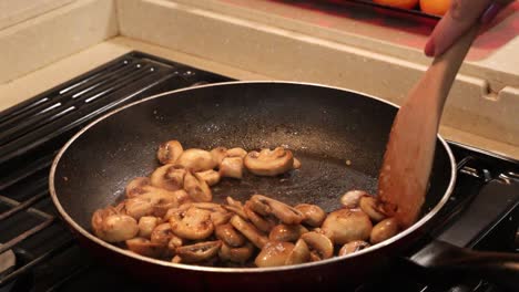 Close-up-of-woman-stirring-sliced-button-mushrooms-to-saute-in-butter-in-a-skillet-in-a-tiny-home-kitchen