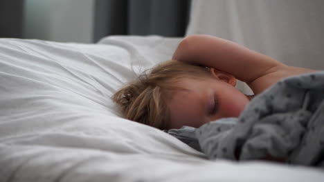 Close-pan-shot-of-young-blonde-boy-with-rosy-cheeks-sleeping-in-bed