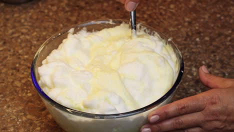 Hand-mixing-eggs-with-spoon-in-a-bowl-for-delicious-sponge-cake-recipe,-close-up