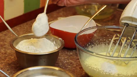 Hand-adding-flour-with-spoon-to-mixed-egg-yolk,-preparation-of-sponge-cake,-closeup