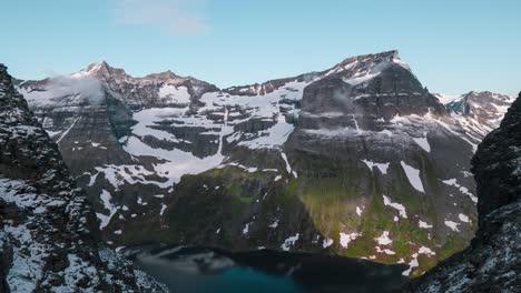 Time-lapse-of-a-beautiful-scenic-view-on-mountain-peaks-covered-with-snow,-down-in-the-valley-a-lake-covered-in-the-mountains-shadow