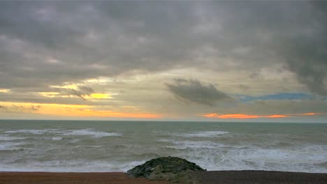The-grey-ocean-meets-the-shingle-beach-under-a-heavy-sky-tinged-orange-by-the-setting-sun