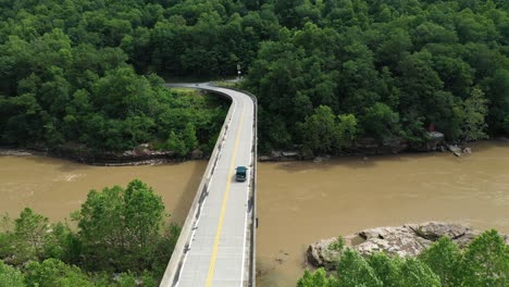 Following-Aerial-View-of-Dark-Van-on-Bridge-Crossing-River-and-Railway-in-Countryside-of-West-Virginia,-USA,-Cinematic-Drone-Shot