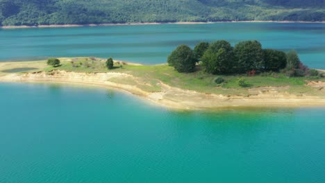 Small-island-with-tree-group-in-Rama-Lake-Bosnia-and-Herzegovina,-Aerial-flyover-shot