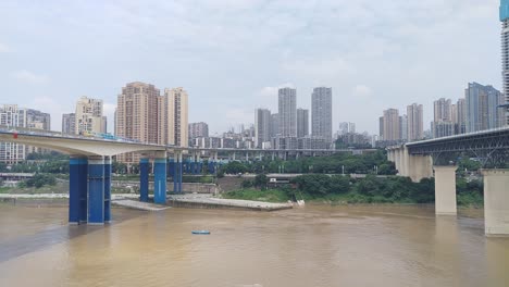 Landscape-clip-of-train-rails-over-a-river-with-a-train-passing-with-the-city-of-Chongqing-,-China-in-the-background