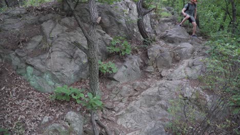 Male-Hiker-Walking-Down-A-Rocky-Mountain-With-Narrow-Path---Medium-Shot