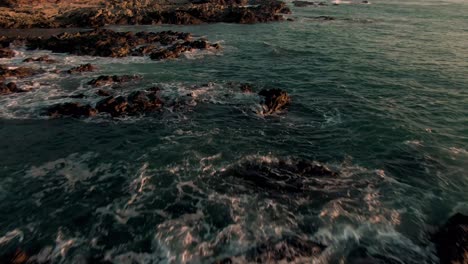 Drone-parallax-flight-above-breaking-swell-on-rocky-Costa-Rica-beach-in-sunset