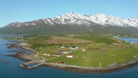 Aerial-view-around-a-small-village-on-the-coast-of-the-Barents-sea,-snowy-mountains-in-the-background,-sunny,-summer-day,-in-Troms,-Nordland,-North-Norway---orbit,-drone-shot