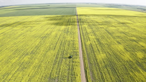 Tractor-Agrícola-Rociando-Los-Campos-De-Canola-Amarilla-En-Un-Hermoso-Día-En-Saskatchewan,-Canadá