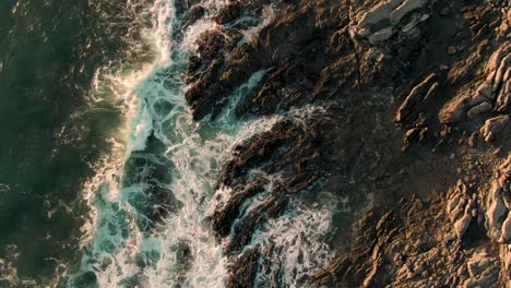 Drone-top-down-crane-shot-of-breaking-waves-on-rocky-Costa-Rica-beach-in-sunset