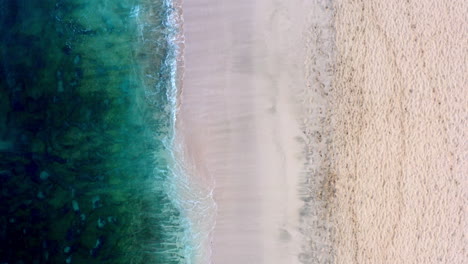 Aerial-shot-of-an-empty-sandy-beach-with-gentle-waves-hitting-the-coastline
