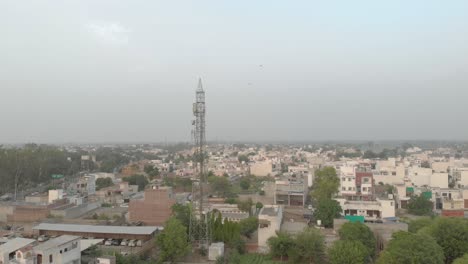 Ein-Taubenschwarm-Fliegt-Am-Blauen-Himmel-Um-Den-Mobilen-Turm-Herum,-Der-In-Einem-Wohngebiet-Der-Stadt-In-Punjab-Steht