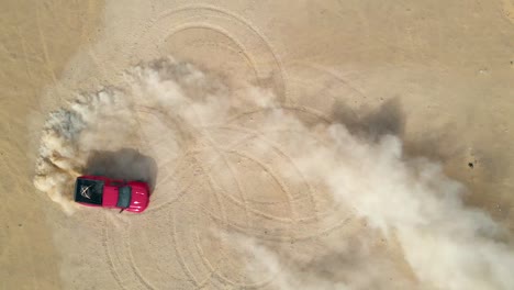 Red-truck-making-doughnuts-in-the-desert-sand,-aerial-top-down-view