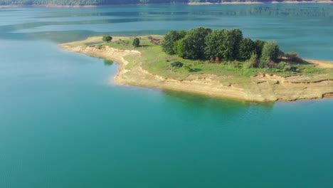 Lago-Rama-En-Bosnia-Y-Herzegovina-Con-Isla-Erosionada-Con-Un-Grupo-De-árboles,-Toma-Aérea-De-Carro