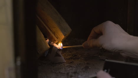 Close-up-of-old-elderly-Caucasian-woman-lady-grandma-hands-lighting-a-wooden-match-to-light-a-cozy-warm-fire-in-a-fireplace-oven-stove-in-a-cabin-during-snowy-cold-Christmas-xmas-celebration-warmth
