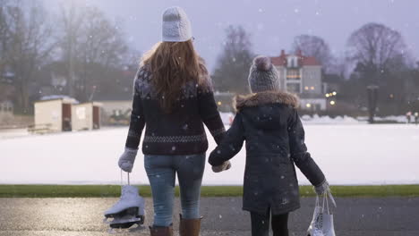 Middle-aged-mom-and-8-year-old-young-daughter-walks-hand-in-hand-together-on-a-snowy-winters-day-to-the-ice-skating-rink-to-practice-ice-skating-for-bonding-activities-as-a-family-during-Christmas-fun