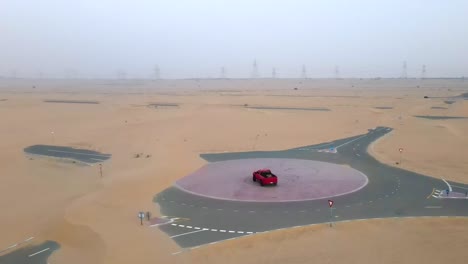 Red-truck-doing-doughnuts-on-an-emptry-road-in-the-desert,-drone-orbiting