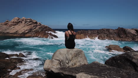 Einsames-Und-Nachdenkliches-Mädchen,-Das-Auf-Dem-Felsen-Sitzt,-Beobachtet-Den-Rauen-Ozean