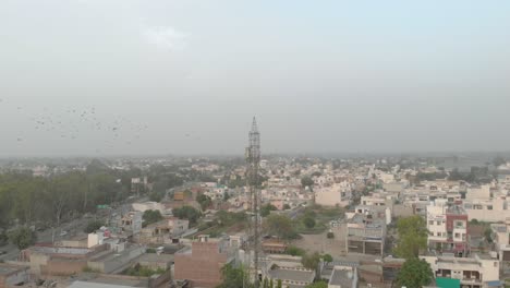 Ein-Taubenschwarm-Fliegt-Am-Blauen-Himmel-Um-Den-Mobilen-Turm-Herum,-Der-In-Einem-Wohngebiet-Der-Stadt-In-Punjab-Steht