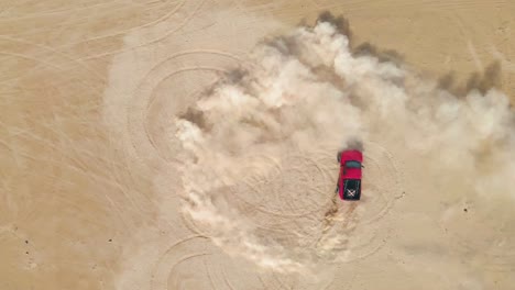 Red-truck-making-doughnuts-in-the-desert-sand,-aerial-top-view