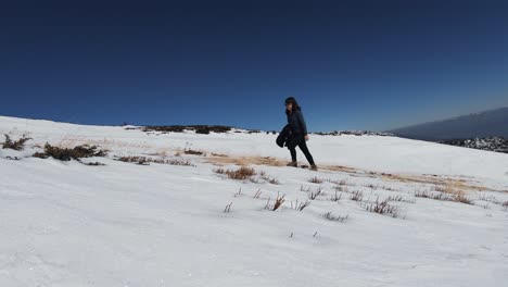 Steady-shot-of-a-girl-slowly-moving-up-a-snowy-mountain-with-a-few-plants-around