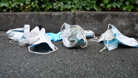 Dirty-discarded-used-corona-virus-masks-blowing-trash-in-wind-on-street-sidewalk-dolly-left-slow