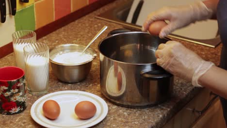 Breaking-eggs-into-a-large-saucepan-with-ingredients-for-flour-and-glasses-of-milk
