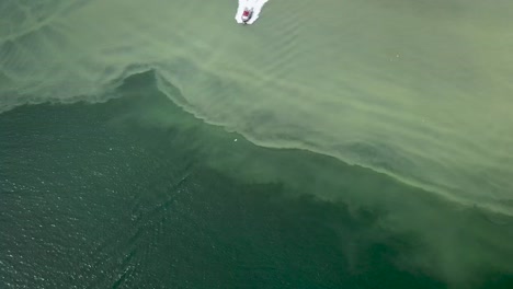 Motorboat-Sailing-Over-The-Blue-Sea-With-Silty-Sea-Bed-Under---aerial-slowmo