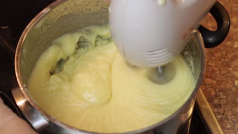 Using-a-handheld-whisk-to-mix-a-boiled-milk-frosting-batter-on-a-stove