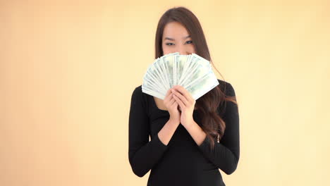 Happy-wealthy-asian-female-hidding-her-face-behind-dollar-cash-bills-in-folding-fan-shape,-full-frame-slow-motion