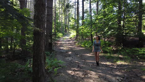 Young-healthy-caucasian-girl-walking-relaxed-inside-a-magical-forest-on-a-sunny-day,-early-summer