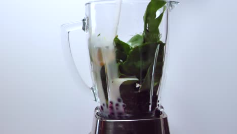 Pouring-milk-on-spinach,-fruits-and-berries,-in-a-blender,-while-making-a-healthy-smoothie---Grey-background---Static-view